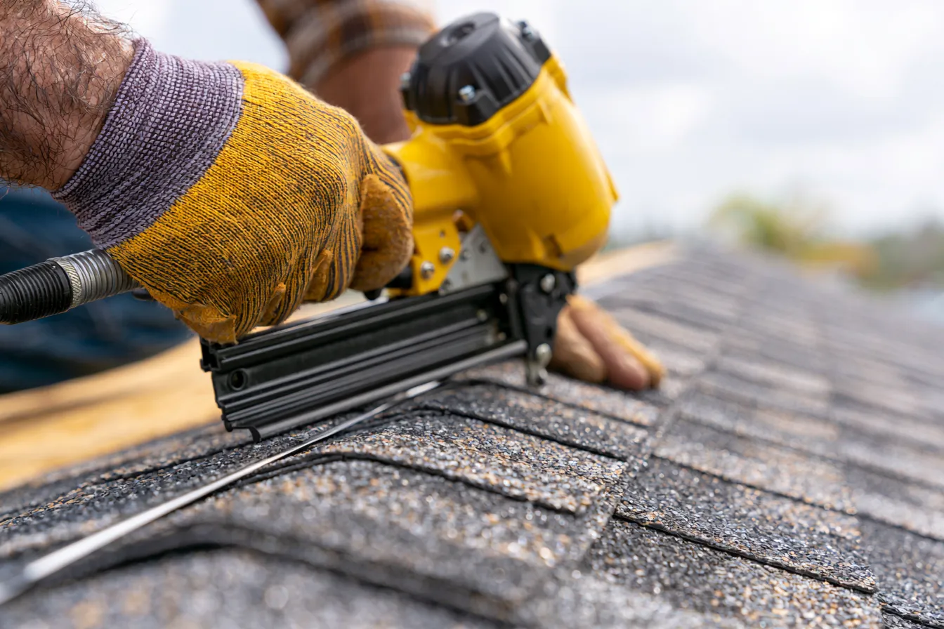 Gloved hands nailing fresh ridge cap shingles