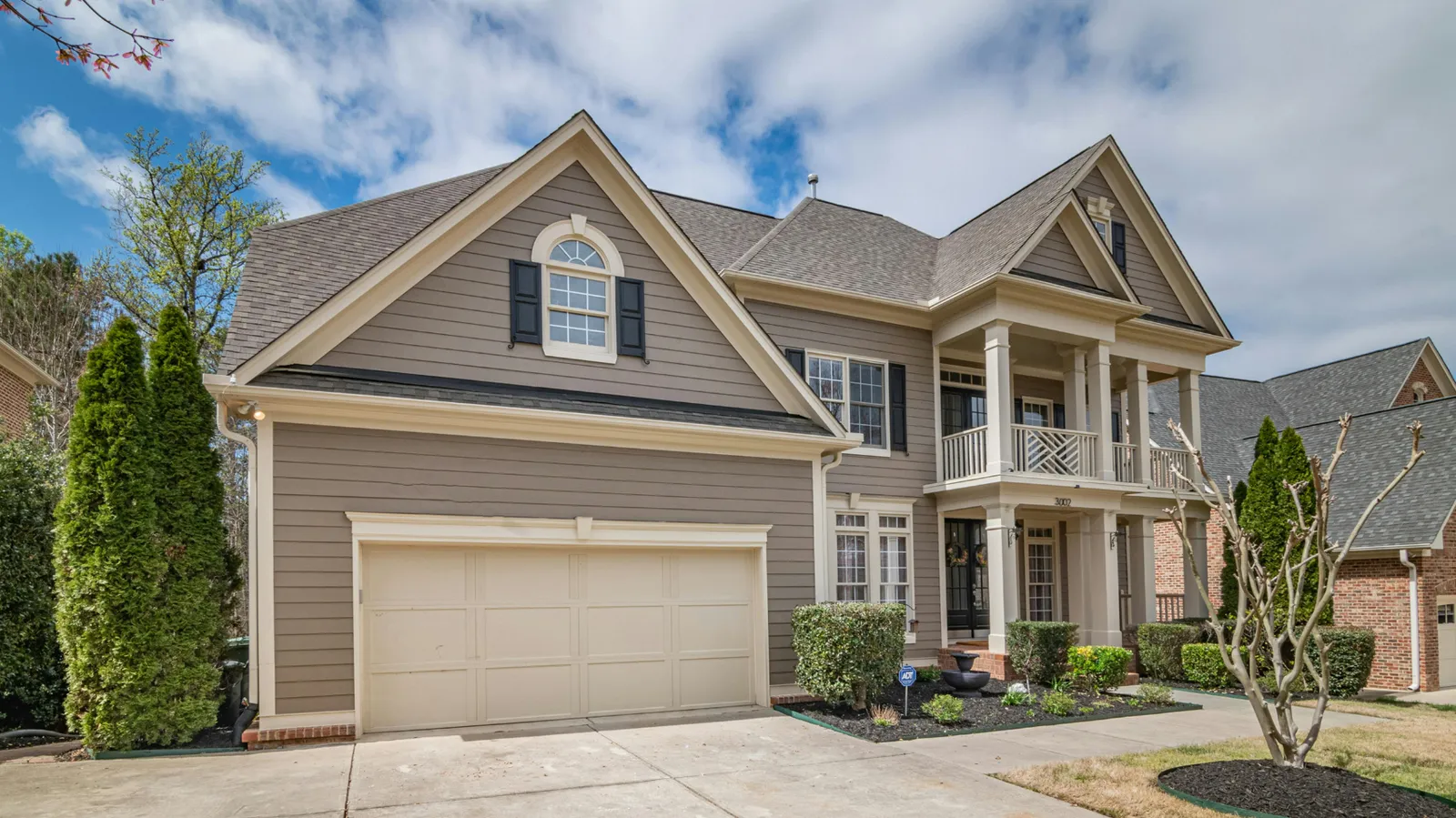 Brown asphalt shingle roof over a tan two-story home with columned balcony