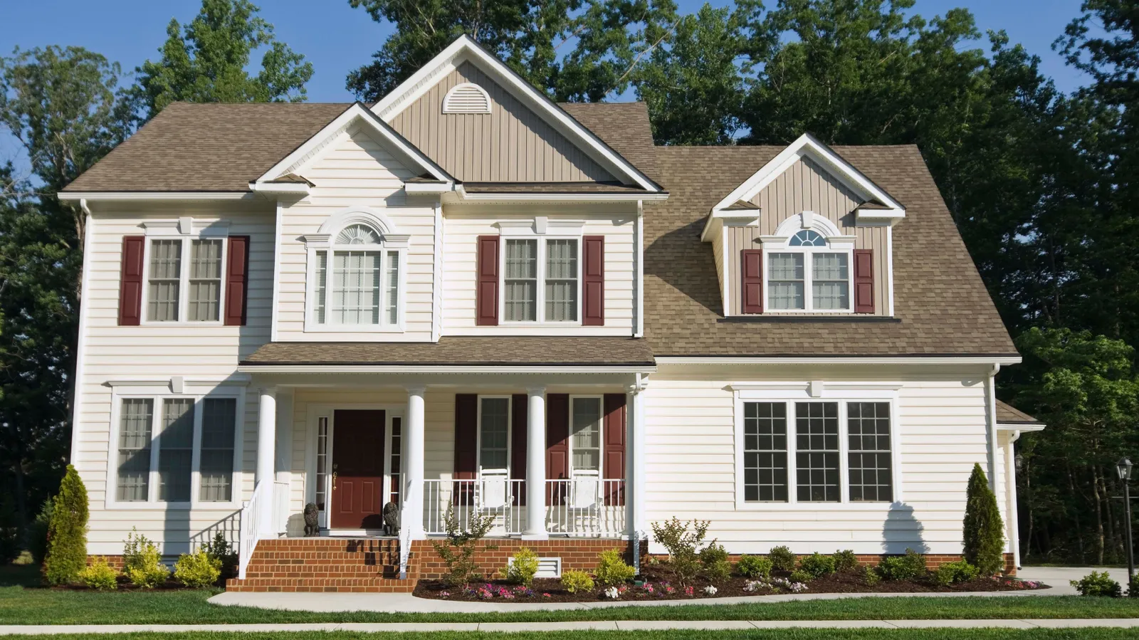 Covered porch on a cream two-story house beneath a brown shingle roof