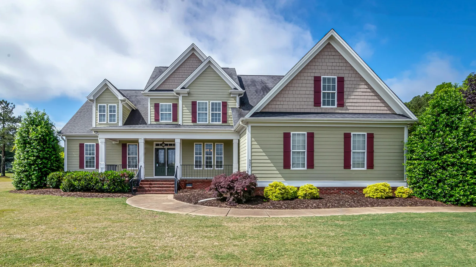 Sage green home with dark shingle roof and red shutters