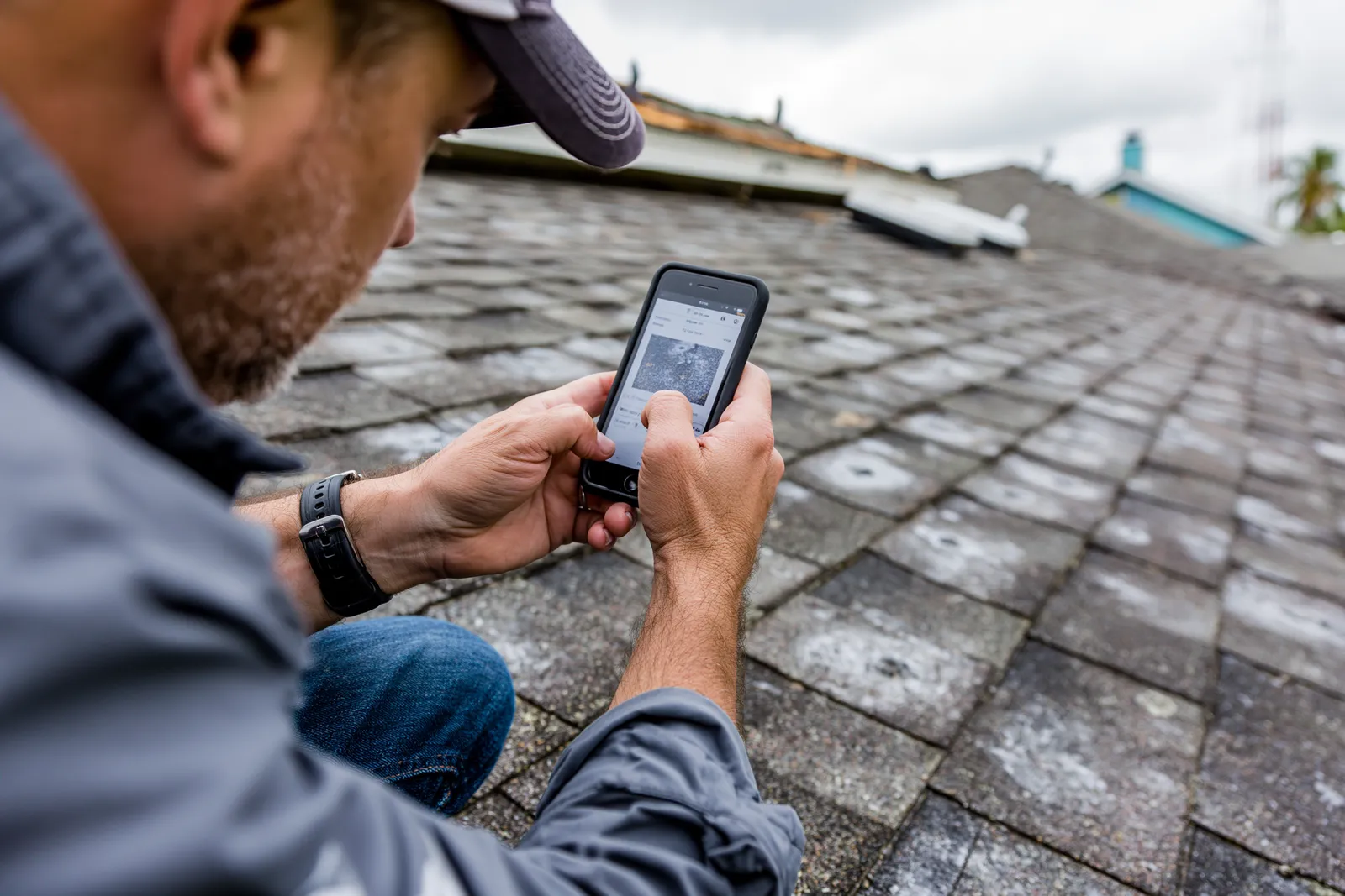 A roofer photographs a weathered shingle roof using a smartphone