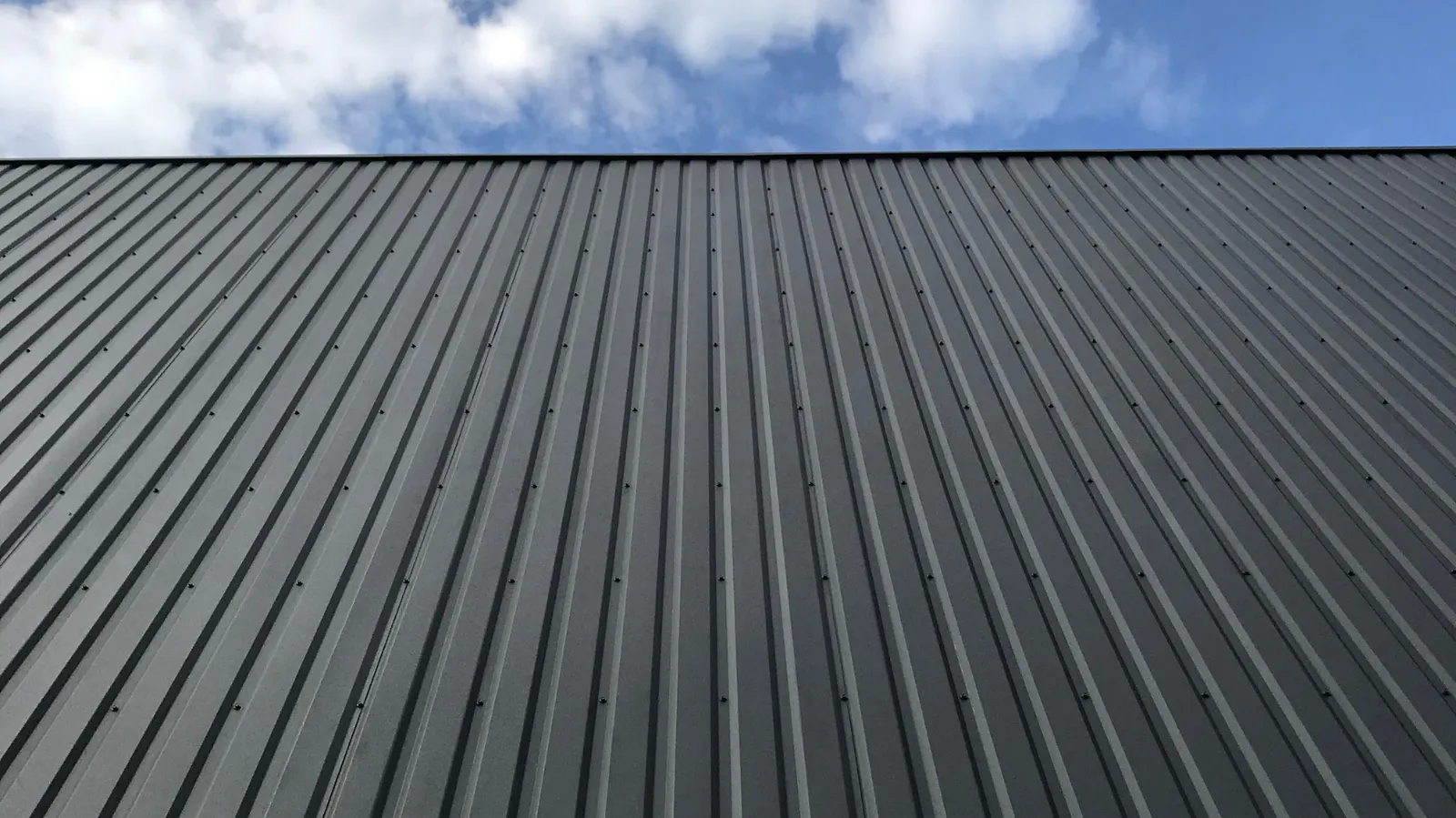 Partly cloudy sky above rising dark ribbed metal panels