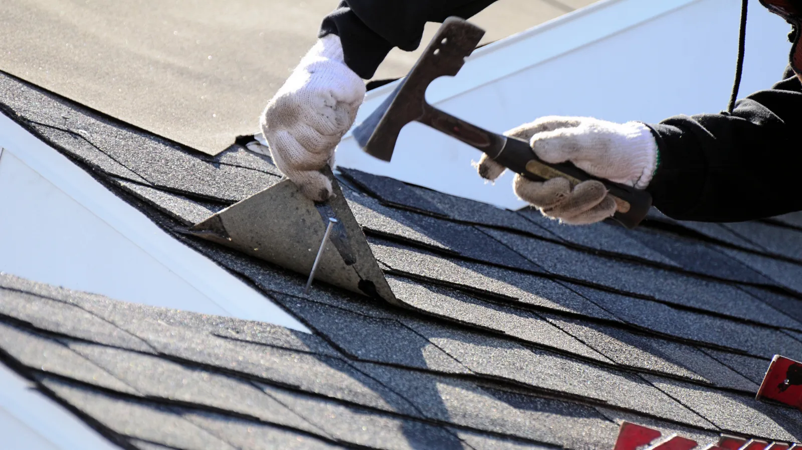 Roofing hammer used by a gloved roofer to nail metal flashing onto shingles